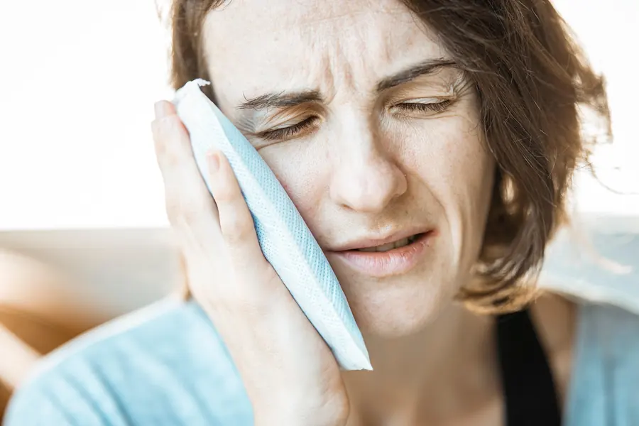 Woman holding an ice pack to her cheek with tooth pain
